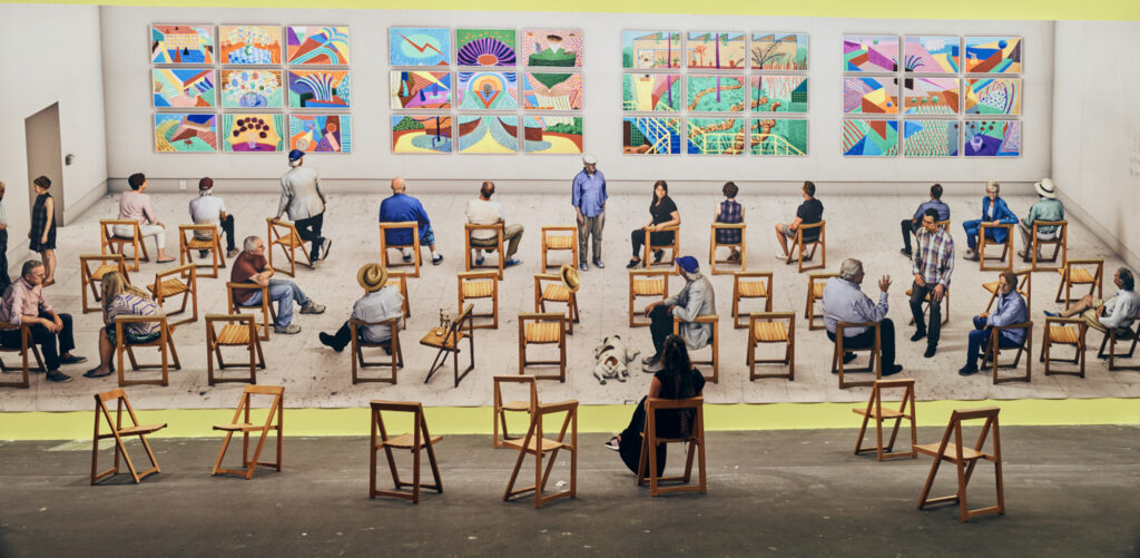 David Hockney art exhibition 2021 socially distanced seating arrangement wooden chairs colourful paintings