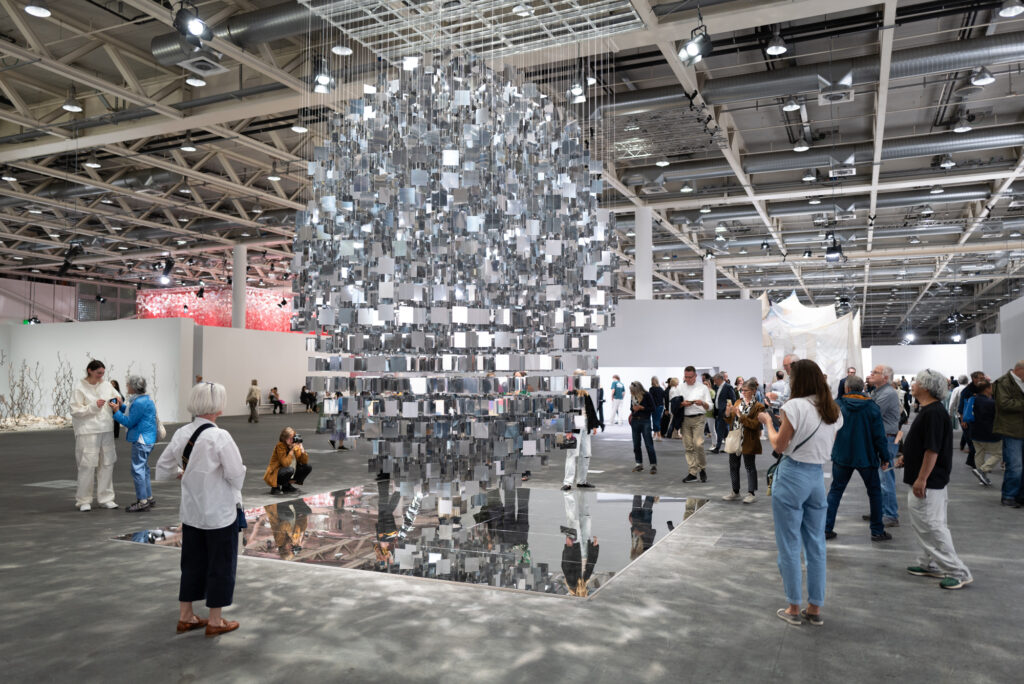 Art Basel 2024 suspended mirror installation with diverse international collectors and visitors viewing contemporary art